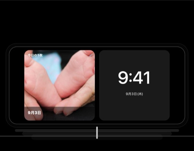 充電台に横向きに置いた iPhone のスタンバイ画面に、時計と今日の1枚が並んでいる